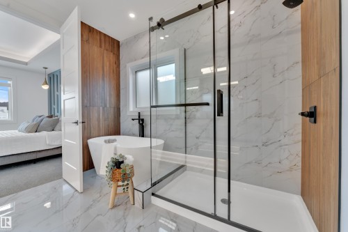 Luxurious bathroom featuring a white freestanding bathtub, a glass-enclosed shower with black fixtures, and white marble-patterned flooring and wall tiles - 110 Eldridge Point(E), St. Albert, AB - Indoor Photo Showing Bathroom