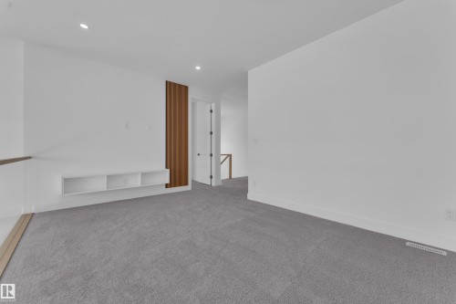 Spacious room featuring light gray carpeting, recessed lighting, white walls, and a built-in media console with open shelving - 110 Eldridge Point(E), St. Albert, AB - Indoor Photo Showing Other Room