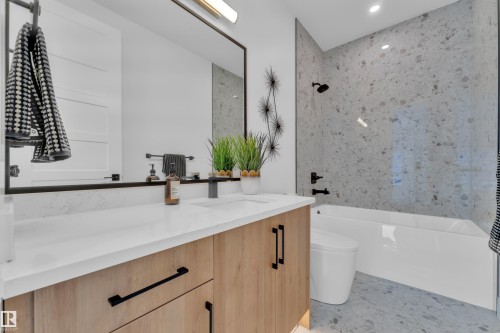 Modern bathroom featuring a single vanity with a light wood finish and white countertop, a black framed mirror, and a white bathtub with a tile surround - 110 Eldridge Point(E), St. Albert, AB - Indoor Photo Showing Bathroom