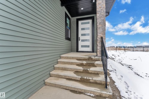 The property features a contemporary front door with horizontal glass panels, a stone pillar, and concrete steps with a black metal handrail - 110 Eldridge Point(E), St. Albert, AB - Outdoor
