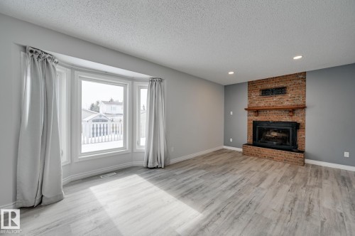 Living area featuring light-colored flooring, a bay window with curtains, and a brick fireplace - 8507 152B Avenue, Edmonton, AB - Indoor Photo Showing Living Room With Fireplace