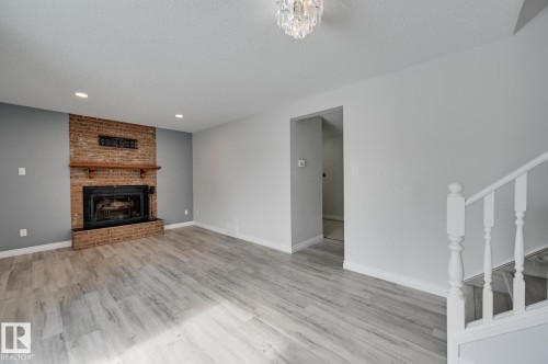 Living area featuring light-toned flooring, a brick fireplace with a wood mantel, and overhead lighting - 8507 152B Avenue, Edmonton, AB - Indoor With Fireplace