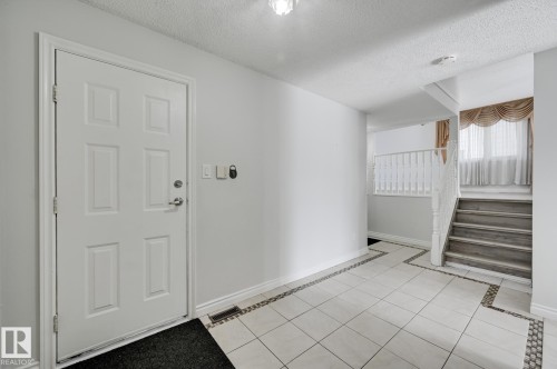 Entryway featuring a white paneled door, light-colored tile flooring with decorative borders, and a staircase with white railings - 8507 152B Avenue, Edmonton, AB - Indoor Photo Showing Other Room