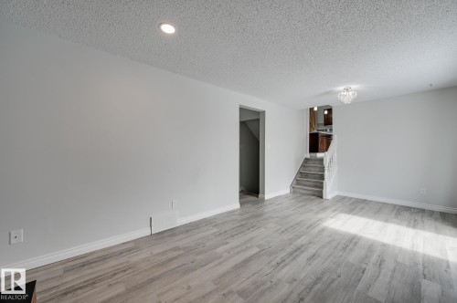 Spacious living area featuring light-toned flooring, white walls, and a decorative light fixture - 8507 152B Avenue, Edmonton, AB - Indoor Photo Showing Other Room
