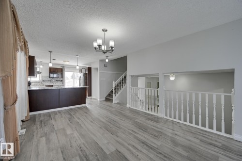 Spacious open concept living area featuring grey wood-look flooring, a modern chandelier, and white banister railing - 8507 152B Avenue, Edmonton, AB - Indoor