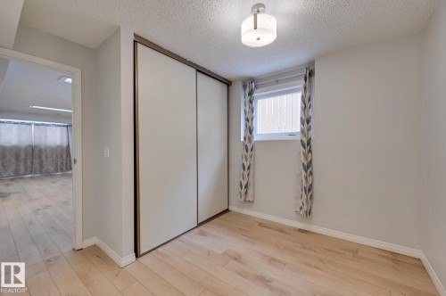 This room features light-toned wood flooring and a window with patterned curtains - 8507 152B Avenue, Edmonton, AB - Indoor Photo Showing Other Room
