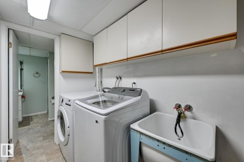 This laundry area features white upper cabinets, a utility sink, and tiled flooring - 8507 152B Avenue, Edmonton, AB - Indoor Photo Showing Laundry Room