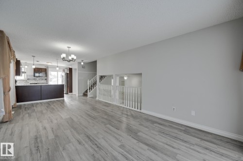 This spacious open-concept area features light grey flooring, freshly painted walls, a modern kitchen with dark cabinetry and stainless steel appliances, and a staircase with white railings - 8507 152B Avenue, Edmonton, AB - Indoor