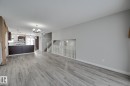 This spacious open-concept area features light grey flooring, freshly painted walls, a modern kitchen with dark cabinetry and stainless steel appliances, and a staircase with white railings - 8507 152B Avenue, Edmonton, AB  - Indoor 