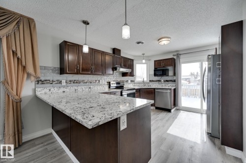 The property features a kitchen with dark wood cabinetry, light-colored countertops with a distinct pattern, and a tile backsplash - 8507 152B Avenue, Edmonton, AB - Indoor Photo Showing Kitchen With Upgraded Kitchen