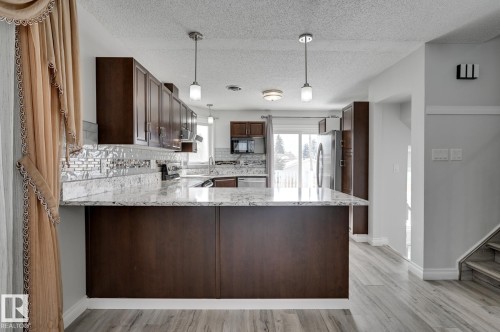 The kitchen features dark wood cabinetry, light-toned granite countertops, and a subway tile backsplash - 8507 152B Avenue, Edmonton, AB - Indoor Photo Showing Kitchen With Upgraded Kitchen