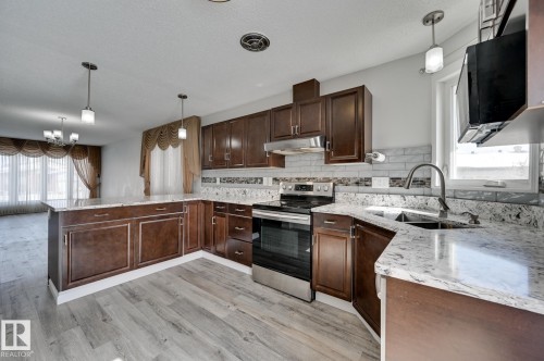 The kitchen features hardwood cabinetry, granite countertops, and stainless steel appliances, with a light gray backsplash and a sink with a gooseneck faucet - 8507 152B Avenue, Edmonton, AB - Indoor Photo Showing Kitchen With Double Sink With Upgraded Kitchen