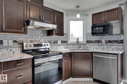 The kitchen features dark wood cabinetry, light-colored granite countertops, and a subway tile backsplash - 8507 152B Avenue, Edmonton, AB - Indoor Photo Showing Kitchen With Stainless Steel Kitchen