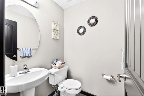 This bathroom features a white pedestal sink with a chrome faucet, a large circular mirror with overhead lighting, and a white toilet - 1121 59A Street, Edmonton, AB - Indoor Photo Showing Bathroom
