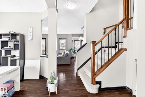 The property features rich hardwood flooring throughout the main living areas, a staircase with carpeting and a wooden banister with black iron balusters, and large windows that provide natural light - 1121 59A Street, Edmonton, AB - Indoor Photo Showing Other Room