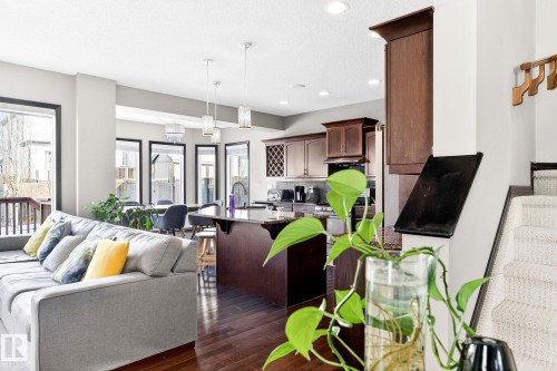 The property features an open-concept living area with hardwood flooring, a spacious kitchen with dark wood cabinetry and a central island, and a dining area with pendant lighting and large windows - 1121 59A Street, Edmonton, AB - Indoor