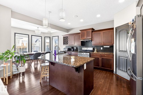 The kitchen features dark wood cabinetry, a granite island countertop, and stainless steel appliances - 1121 59A Street, Edmonton, AB - Indoor Photo Showing Kitchen