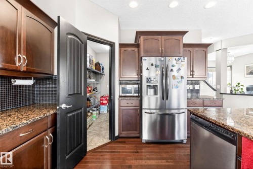 This kitchen features rich wood cabinetry, granite countertops, and a full-size stainless steel refrigerator - 1121 59A Street, Edmonton, AB - Indoor Photo Showing Kitchen