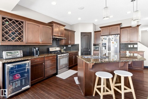 The kitchen features dark wood cabinetry, stainless steel appliances, granite countertops, and an island with seating - 1121 59A Street, Edmonton, AB - Indoor Photo Showing Kitchen