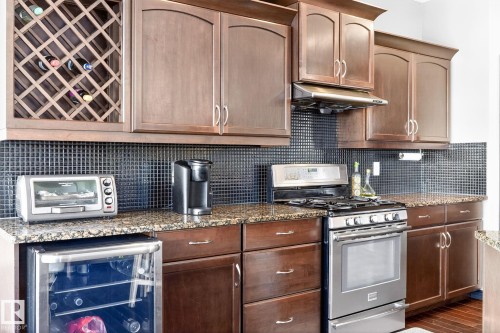 The kitchen features dark wood cabinetry, granite countertops, a dark tiled backsplash, and stainless steel appliances including a range with an oven - 1121 59A Street, Edmonton, AB - Indoor Photo Showing Kitchen
