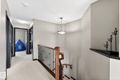 The property features a staircase with a wooden handrail and wrought iron spindles, a light-colored carpeted hallway, and neutral-toned walls - 1121 59A Street, Edmonton, AB - Indoor Photo Showing Other Room