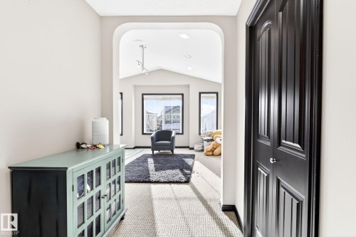 Bright hallway with light-colored walls and a textured carpet, leading to an open living area with large windows, a vaulted ceiling, and recessed lighting - 1121 59A Street, Edmonton, AB - Indoor Photo Showing Other Room
