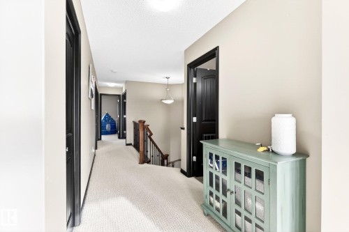 Inviting hallway with neutral wall paint and light-colored carpeting, featuring dark trim around doorways and a wooden staircase with dark metal balusters - 1121 59A Street, Edmonton, AB - Indoor Photo Showing Other Room