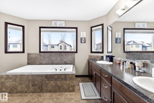 The bathroom features a built-in bathtub with tiled surround, a long vanity with two sinks, and windows providing natural light - 1121 59A Street, Edmonton, AB - Indoor Photo Showing Bathroom