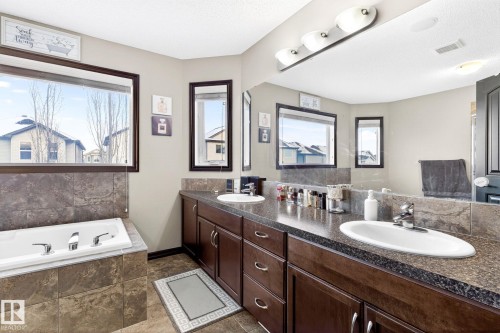 The bathroom features a built-in bathtub with tiled surround, a double vanity with dark wood cabinetry, and a large mirror with overhead lighting - 1121 59A Street, Edmonton, AB - Indoor Photo Showing Bathroom