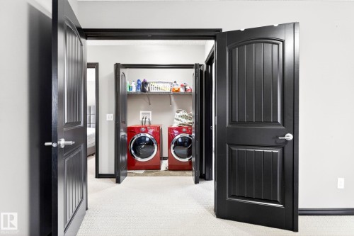 Laundry area featuring red front-loading washer and dryer units, a utility shelf, and carpeted flooring - 1121 59A Street, Edmonton, AB - Indoor Photo Showing Other Room