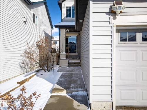 The property features a front entrance with a covered porch and a white pillar, a concrete pathway, and an attached garage with a panelled door and windows - 1121 59A Street, Edmonton, AB - Outdoor