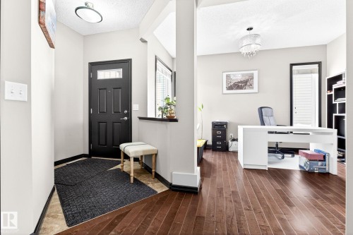 The property features a welcoming entryway with a dark paneled door and light-colored walls, leading to a room with rich hardwood flooring - 1121 59A Street, Edmonton, AB - Indoor Photo Showing Other Room