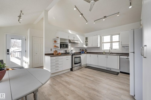 The kitchen features white cabinetry, stainless steel appliances, and dark countertops, complemented by light-toned flooring - 11116 52 Street Nw, Edmonton, AB - Indoor Photo Showing Kitchen