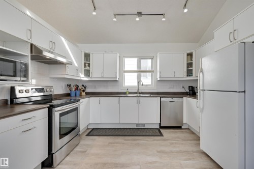 The kitchen features white cabinetry, stainless steel appliances, a white tile backsplash, and light-colored flooring - 11116 52 Street Nw, Edmonton, AB - Indoor Photo Showing Kitchen