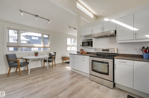 The property features a bright kitchen with white cabinetry, stainless steel appliances, and a tiled backsplash - 11116 52 Street Nw, Edmonton, AB - Indoor Photo Showing Kitchen