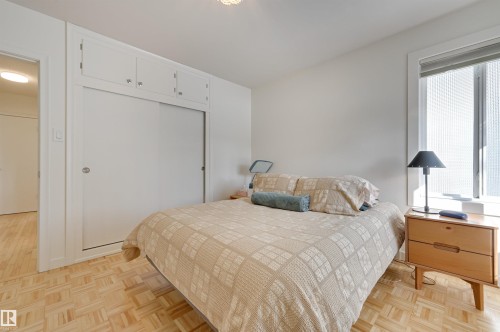 This room features light-toned parquet flooring, a window with vertical blinds, and a built-in closet with overhead cabinetry - 11116 52 Street Nw, Edmonton, AB - Indoor Photo Showing Bedroom