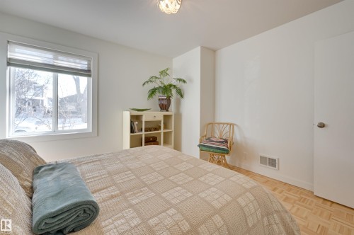 The room features light-colored walls and hardwood flooring, a window providing natural light, and a white door with a round knob - 11116 52 Street Nw, Edmonton, AB - Indoor Photo Showing Bedroom