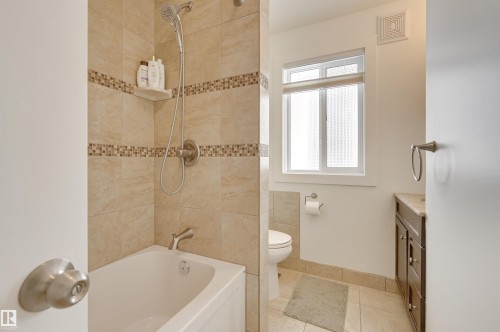 Bathroom featuring a bathtub and shower with tiled walls, a window, and a vanity with a sink - 11116 52 Street Nw, Edmonton, AB - Indoor Photo Showing Bathroom