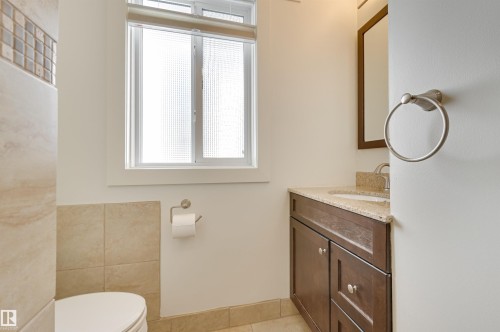 The property features a bathroom with a window, a vanity with a dark wood cabinet and a light-colored countertop, and a toilet - 11116 52 Street Nw, Edmonton, AB - Indoor Photo Showing Bathroom