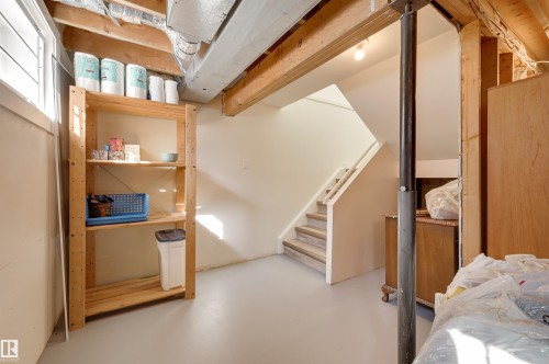 The property features an unfinished space with exposed ceiling joists and ductwork, a window for natural light, and stairs with painted risers and natural wood treads - 11116 52 Street Nw, Edmonton, AB - Indoor