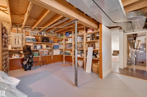 The property features a utility area with exposed ceiling joists and ductwork, a painted concrete floor, and built-in shelving providing extensive storage solutions - 11116 52 Street Nw, Edmonton, AB - Indoor Photo Showing Basement