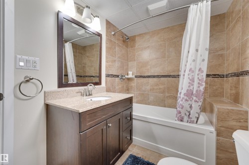 Bathroom featuring a dark wood vanity with a light-colored countertop, a mirror, and a shower-tub combination with light-toned tiled walls - 11116 52 Street Nw, Edmonton, AB - Indoor Photo Showing Bathroom