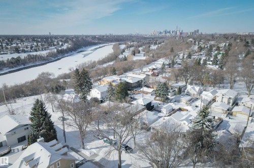 An aerial view of the surrounding residential area featuring snow-covered rooftops, mature trees, and a distant city skyline, with a frozen river visible in the landscape - 11116 52 Street Nw, Edmonton, AB - Outdoor With View