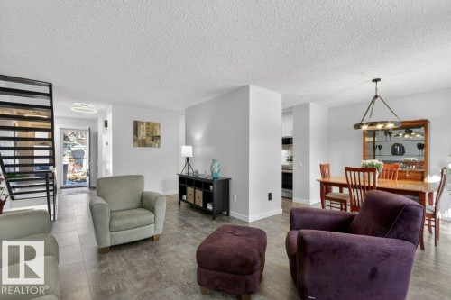 The property features an open-concept living area with luxury vinyl tile flooring, a staircase with black railings, and a dining area illuminated by an overhead chandelier - 91 Hearthstone, Edmonton, AB - Indoor Photo Showing Living Room