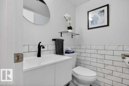 The guest bathroom features a modern vanity with a white countertop and a black faucet, complemented by a round mirror - 91 Hearthstone, Edmonton, AB - Indoor Photo Showing Bathroom