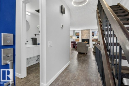 Entryway featuring a staircase with wood treads and a metal railing, vinyl tile flooring, and a view into a living room with a fireplace - 91 Hearthstone, Edmonton, AB - Indoor Photo Showing Other Room