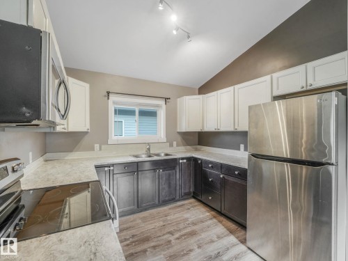 The kitchen features a stainless steel refrigerator, dark base cabinets, white upper cabinets, and a window above the sink - 5035 51 Avenue, Lamont, AB - Indoor Photo Showing Kitchen With Stainless Steel Kitchen With Double Sink