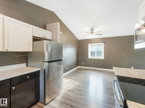 The kitchen features a stainless steel refrigerator and stove, white upper cabinets, and dark lower cabinets with a light-colored countertop - 5035 51 Avenue, Lamont, AB - Indoor Photo Showing Kitchen