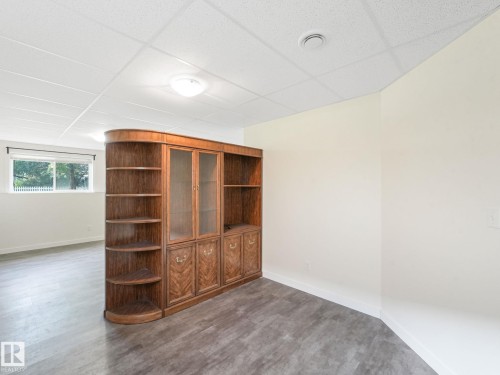 This room features a built-in wooden cabinet with glass doors and shelving, light-colored walls, and a window providing natural light - 5035 51 Avenue, Lamont, AB - Indoor Photo Showing Other Room