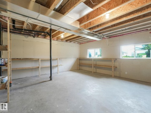 Spacious unfinished basement with exposed wooden ceiling joists, two windows, and built-in shelving - 5035 51 Avenue, Lamont, AB - Indoor Photo Showing Basement